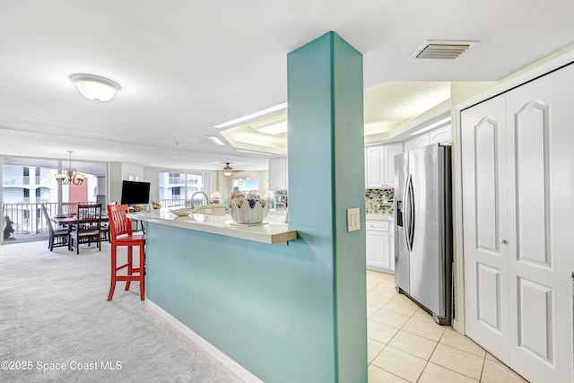 kitchen with visible vents, white cabinets, stainless steel fridge with ice dispenser, a breakfast bar, and light countertops