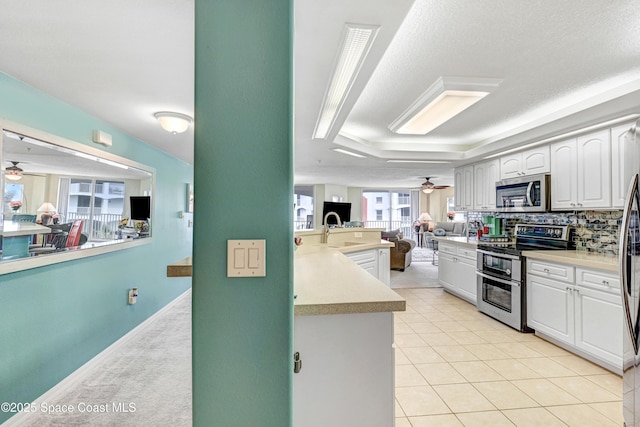 kitchen with a raised ceiling, stainless steel appliances, a ceiling fan, and open floor plan