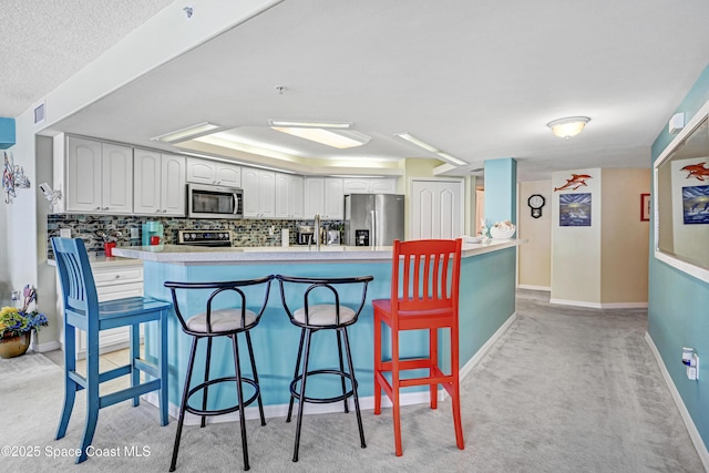 kitchen featuring stainless steel appliances, white cabinets, a kitchen breakfast bar, light countertops, and tasteful backsplash