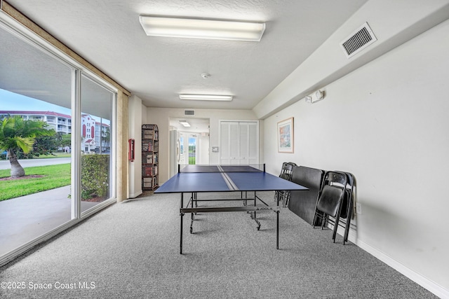 recreation room featuring carpet floors, visible vents, a textured ceiling, and baseboards