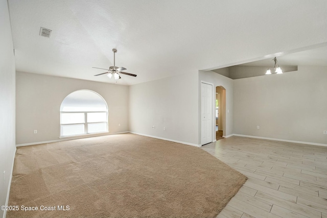 empty room with arched walkways, ceiling fan with notable chandelier, visible vents, and baseboards