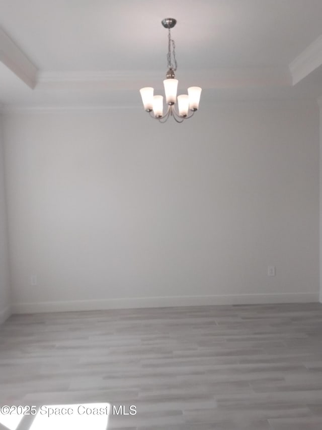 empty room featuring baseboards, ornamental molding, light wood-style flooring, and an inviting chandelier