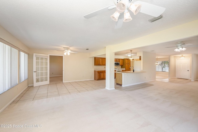 unfurnished living room featuring ceiling fan with notable chandelier, visible vents, a textured ceiling, and light colored carpet