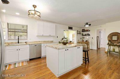 kitchen with light wood finished floors, white cabinets, dishwasher, a kitchen island, and a sink