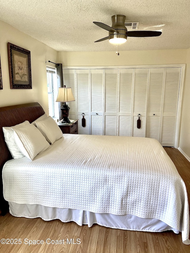 bedroom with a textured ceiling, a closet, visible vents, and wood finished floors