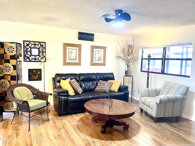 living area with a textured ceiling, ceiling fan, light wood finished floors, and baseboards