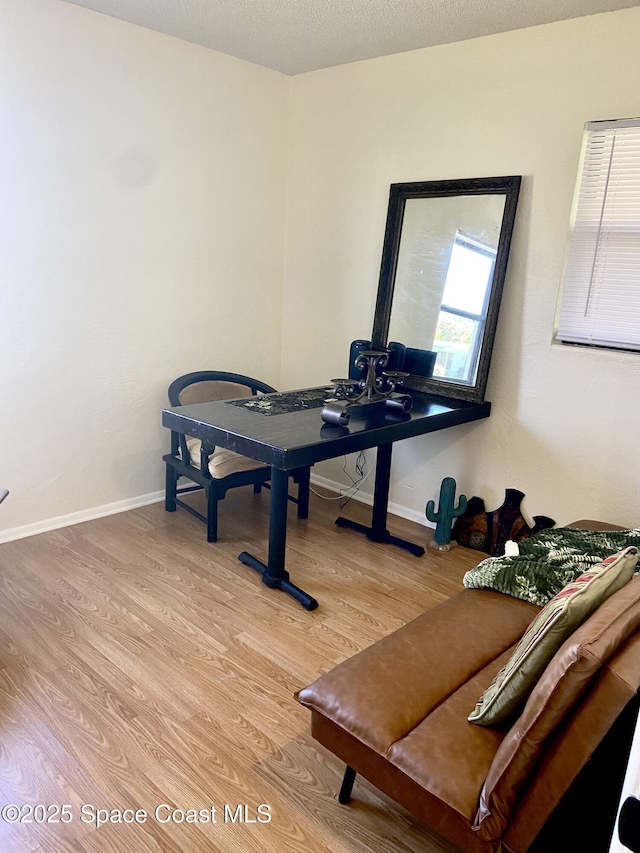 workout room featuring light wood-style floors, a textured ceiling, and baseboards