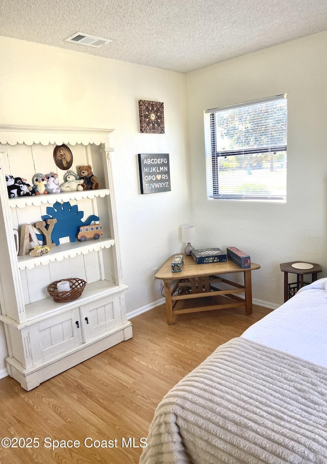 bedroom featuring visible vents, a textured ceiling, baseboards, and wood finished floors