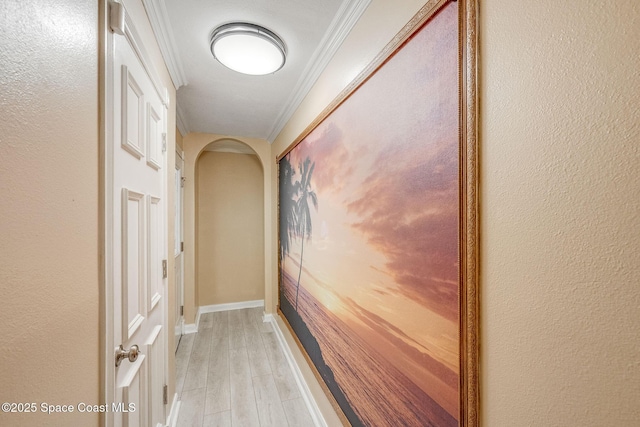 corridor featuring light wood-style flooring, arched walkways, baseboards, and ornamental molding