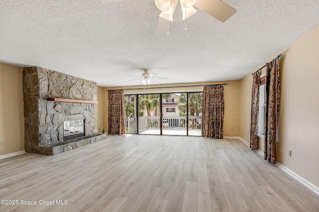 unfurnished living room featuring ceiling fan, a stone fireplace, a textured ceiling, wood finished floors, and baseboards