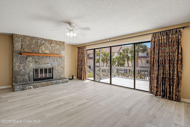 unfurnished living room with a textured ceiling, ceiling fan, a stone fireplace, wood finished floors, and baseboards