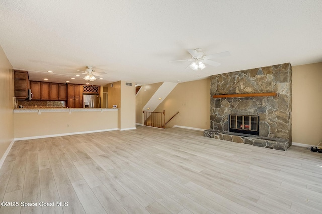 unfurnished living room with a fireplace, light wood-style floors, ceiling fan, a textured ceiling, and baseboards