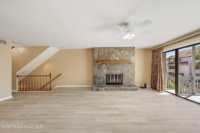 unfurnished living room featuring a textured ceiling, visible vents, wood finished floors, and a stone fireplace