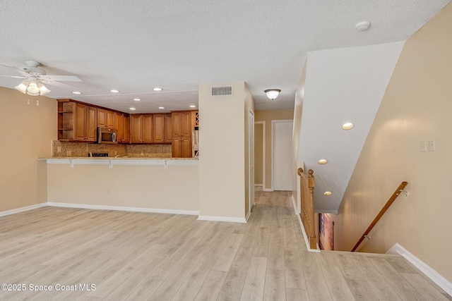 living area featuring light wood finished floors, recessed lighting, visible vents, a textured ceiling, and baseboards