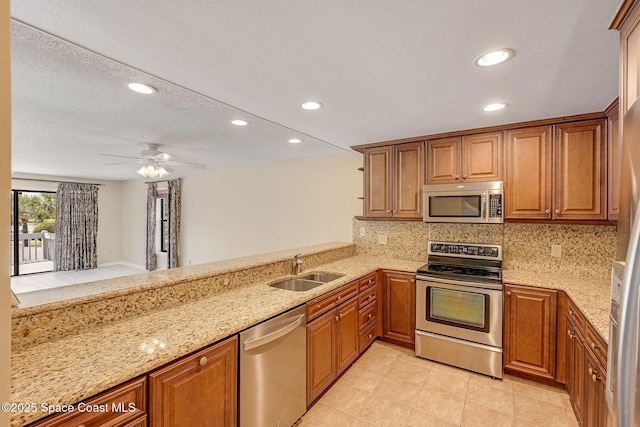 kitchen featuring light stone counters, stainless steel appliances, a sink, tasteful backsplash, and brown cabinetry