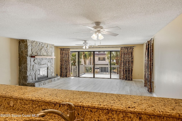 unfurnished living room with a textured ceiling, a fireplace, a ceiling fan, and wood finished floors