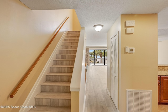 staircase featuring visible vents, a textured ceiling, and wood finished floors