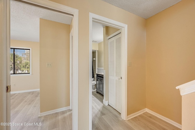 hallway with light wood finished floors, baseboards, and a textured ceiling