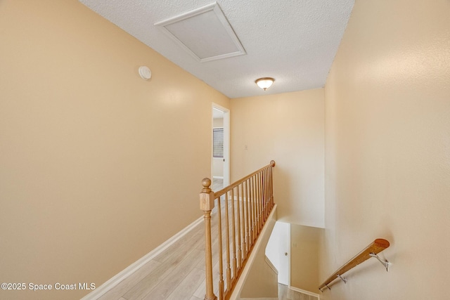 corridor featuring attic access, a textured ceiling, an upstairs landing, light wood-type flooring, and baseboards