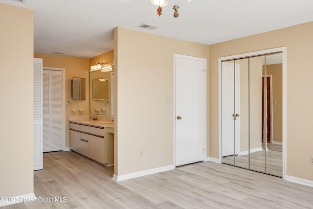 unfurnished bedroom with visible vents, ensuite bath, light wood-style flooring, and baseboards