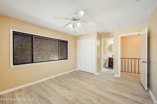 unfurnished bedroom featuring a textured ceiling, a closet, light wood-style flooring, and baseboards