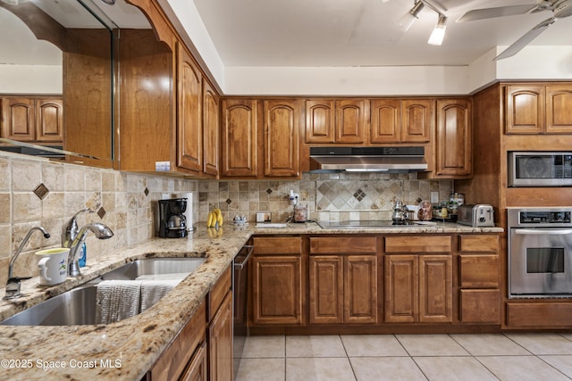 kitchen featuring under cabinet range hood, a sink, appliances with stainless steel finishes, backsplash, and light stone countertops