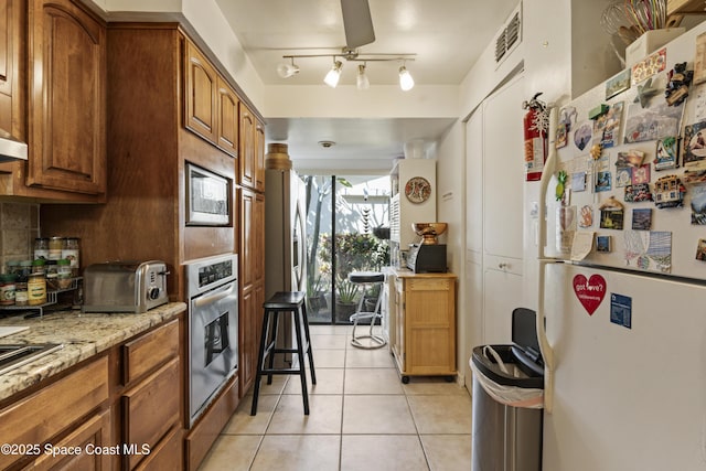 kitchen with a toaster, tasteful backsplash, brown cabinets, stainless steel appliances, and light tile patterned flooring