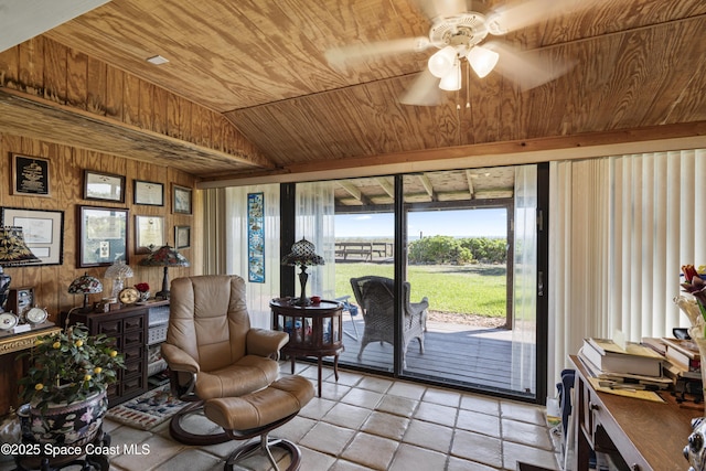 living area with lofted ceiling, wooden ceiling, a ceiling fan, and wooden walls