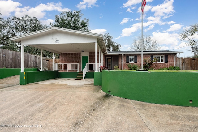 view of front facade with fence, an attached carport, concrete driveway, and brick siding