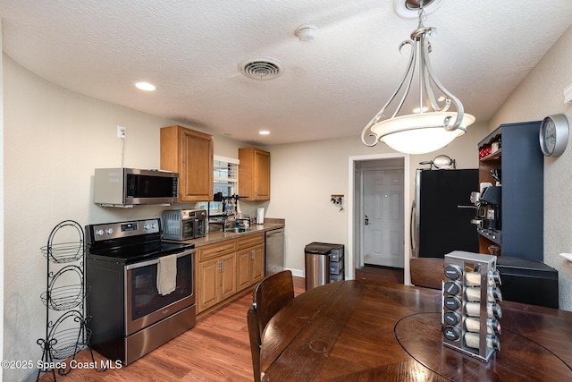 kitchen with visible vents, light wood-style flooring, appliances with stainless steel finishes, brown cabinetry, and a sink