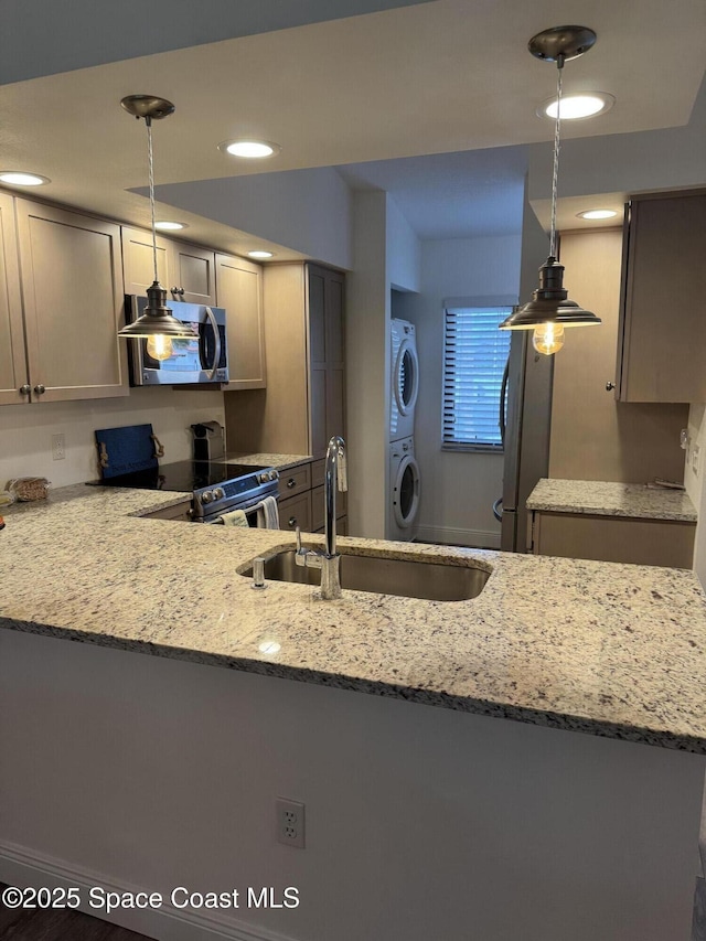 kitchen featuring stacked washer / dryer, light stone countertops, stainless steel appliances, pendant lighting, and a sink