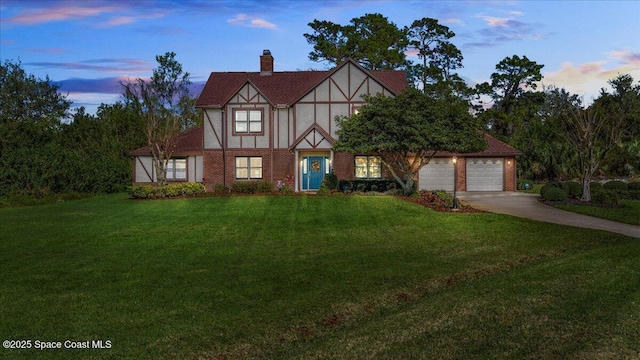 tudor house with brick siding, a chimney, concrete driveway, a front yard, and a garage