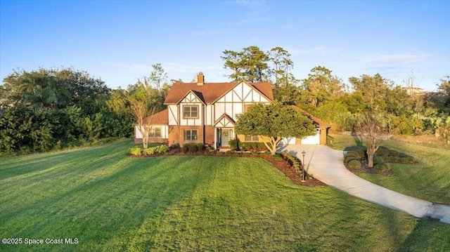 tudor-style house featuring concrete driveway, a chimney, a front yard, and stucco siding