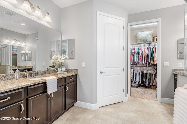 full bath featuring visible vents, a walk in closet, vanity, and baseboards