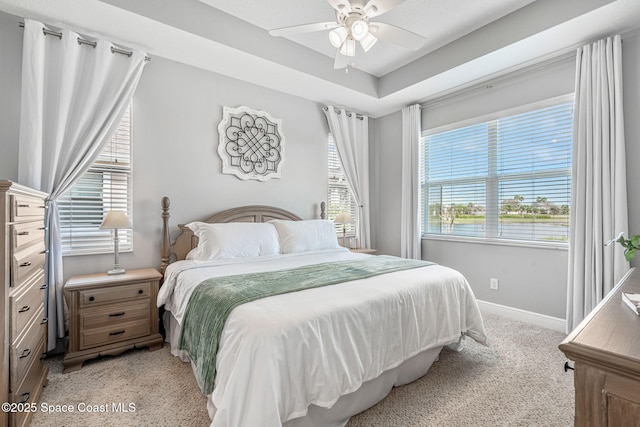 bedroom featuring baseboards, ceiling fan, a raised ceiling, and light colored carpet