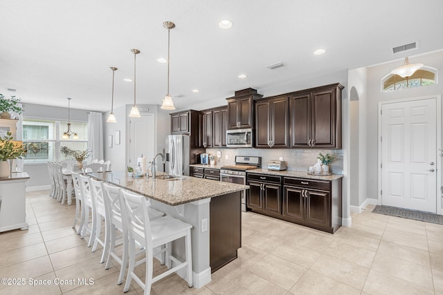 kitchen featuring arched walkways, dark brown cabinetry, stainless steel appliances, a kitchen breakfast bar, and tasteful backsplash