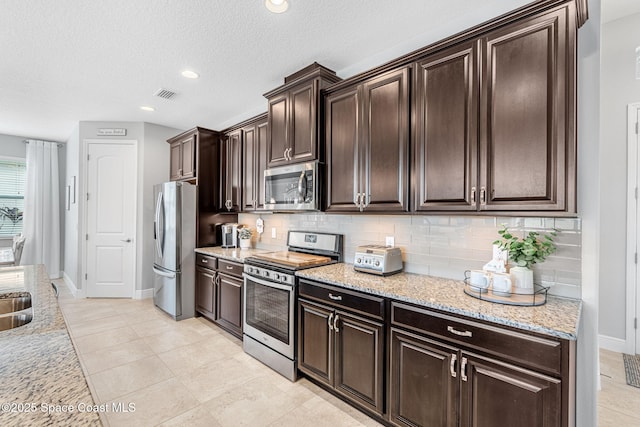 kitchen with dark brown cabinets, appliances with stainless steel finishes, visible vents, and decorative backsplash