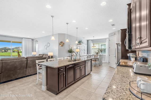 kitchen featuring arched walkways, a sink, visible vents, stainless steel dishwasher, and a center island with sink