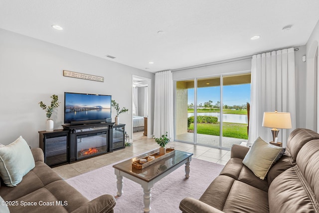 living room featuring light tile patterned floors, a glass covered fireplace, visible vents, and recessed lighting