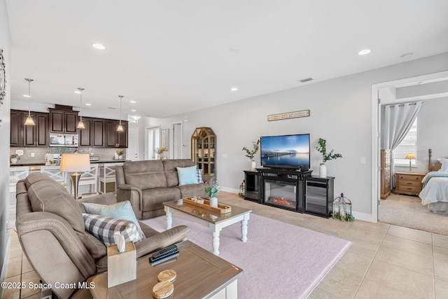 living area featuring light tile patterned floors, visible vents, baseboards, a glass covered fireplace, and recessed lighting