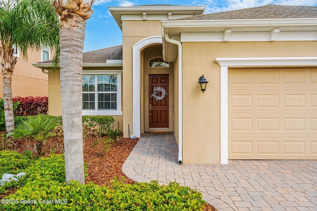 doorway to property with a garage, roof with shingles, and stucco siding