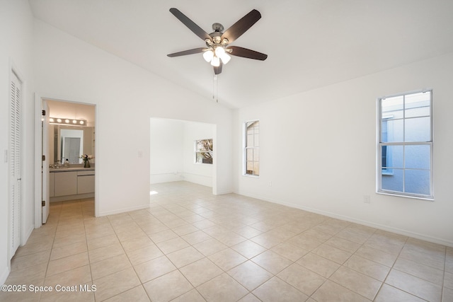 empty room with high vaulted ceiling, light tile patterned floors, baseboards, and ceiling fan