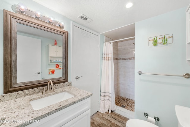 full bath with toilet, tiled shower, wood finished floors, and visible vents