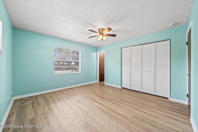 unfurnished bedroom with a textured ceiling, wood finished floors, a ceiling fan, baseboards, and a closet