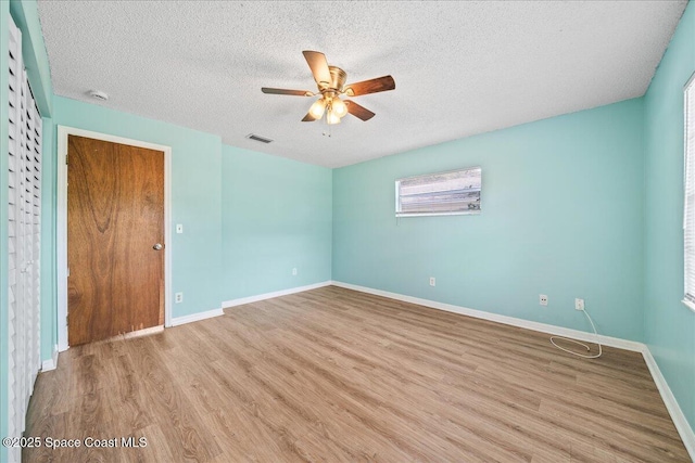 empty room featuring a textured ceiling, ceiling fan, wood finished floors, visible vents, and baseboards