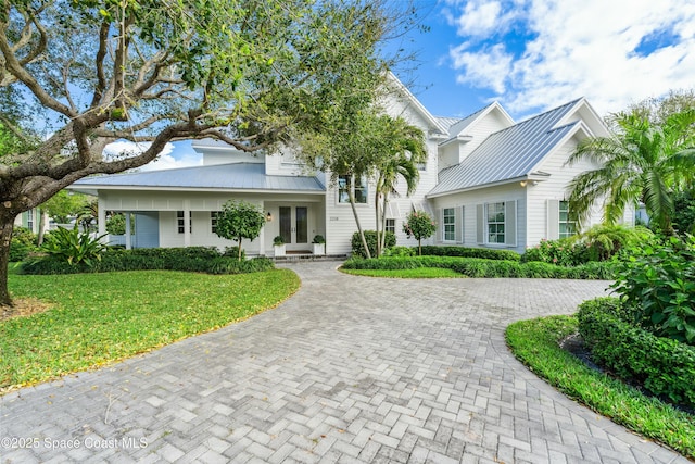 view of front facade featuring a front lawn, metal roof, decorative driveway, and french doors