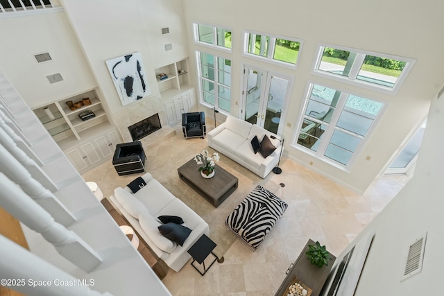 tiled living room featuring built in shelves, visible vents, a towering ceiling, and a premium fireplace