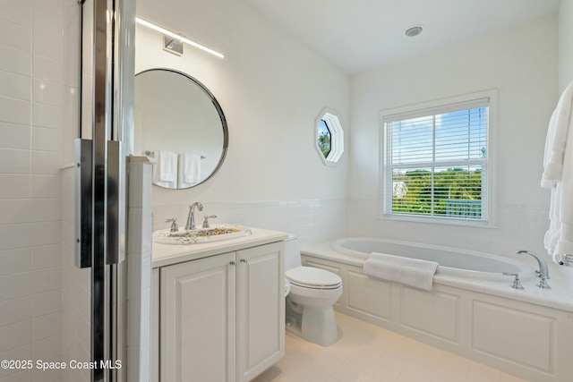 full bath featuring a garden tub, toilet, a wainscoted wall, vanity, and tile walls