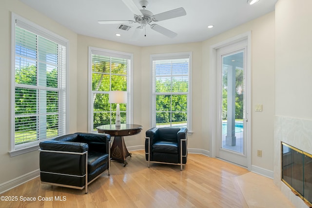 living area with wood finished floors, a healthy amount of sunlight, visible vents, and a premium fireplace