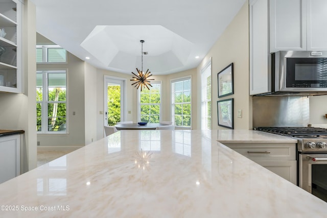 kitchen with light stone counters, a notable chandelier, a raised ceiling, appliances with stainless steel finishes, and white cabinetry